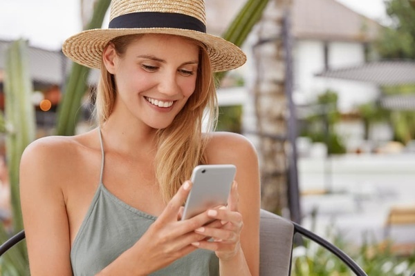 a woman wearing a straw hat is smiling while looking at her phone