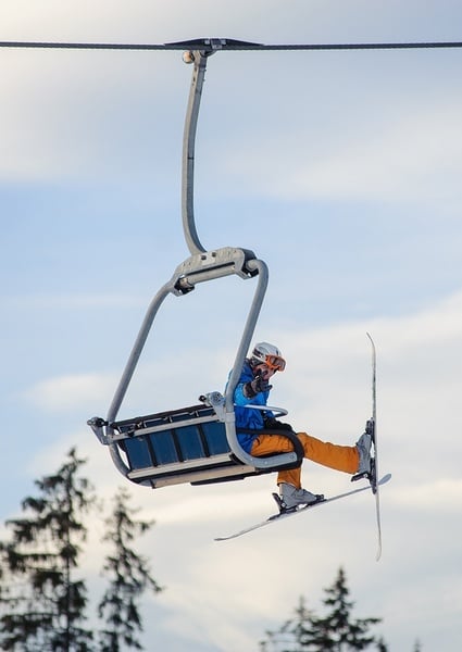 un esquiador se sienta en un telesquí y sostiene una tabla de snowboard