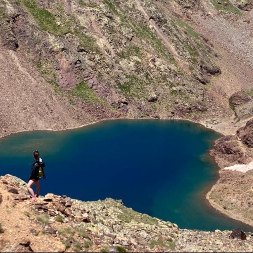 une femme avec un sac à dos se tient au bord d' un lac de montagne