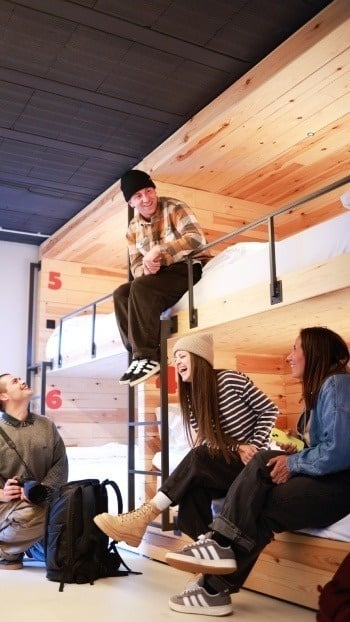 Plusieurs jeunes amis rient et conversent joyeusement dans une chambre à lits superposés en bois.