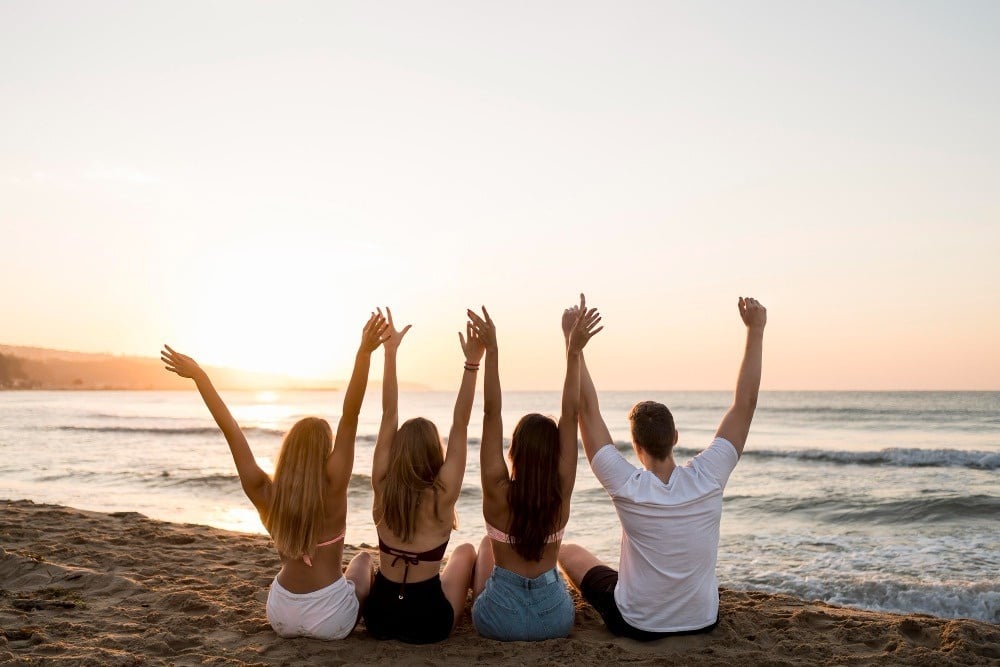 un grupo de personas se sienta en la playa con las manos en el aire