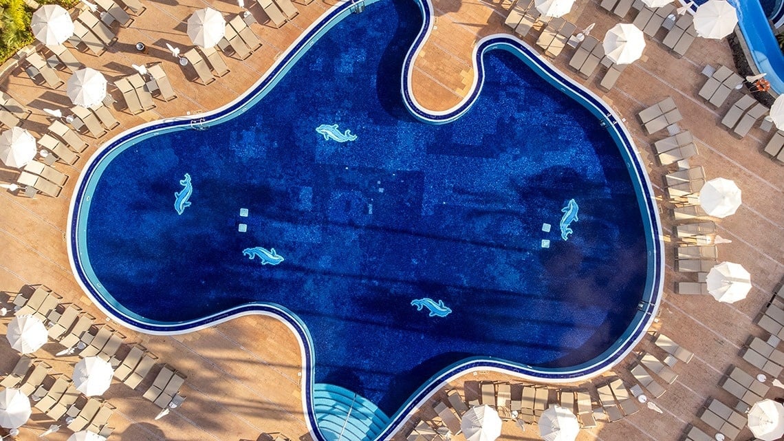 una vista aérea de una piscina en forma de pez rodeada de sillas y sombrillas
