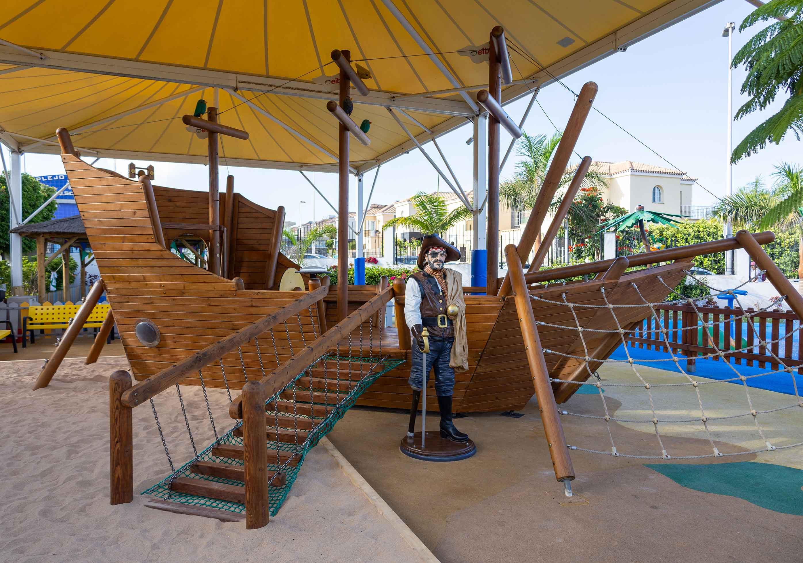 Kinderfreundlicher Spielbereich mit Piratenschiff, Landmar, und Kletterseilnetz im Freien.