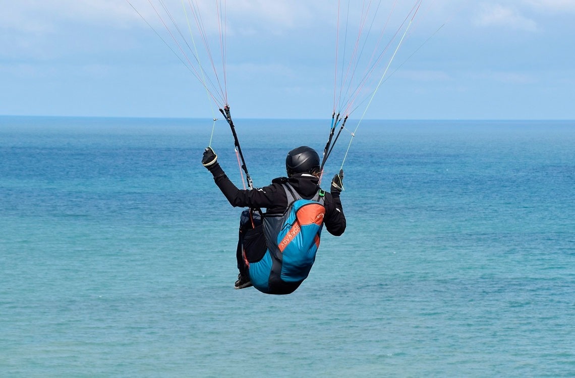 ein Mann fliegt mit einem Drachen über das Meer