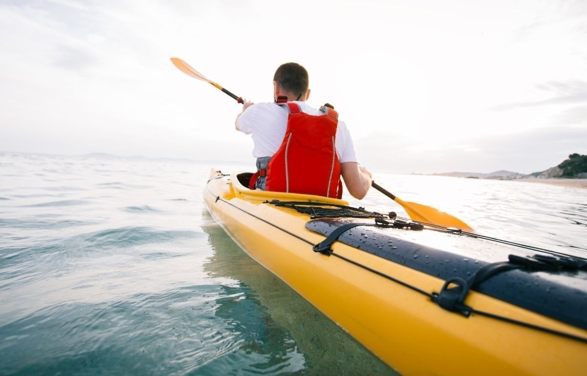 un hombre con una mochila roja rema un kayak amarillo en el océano
