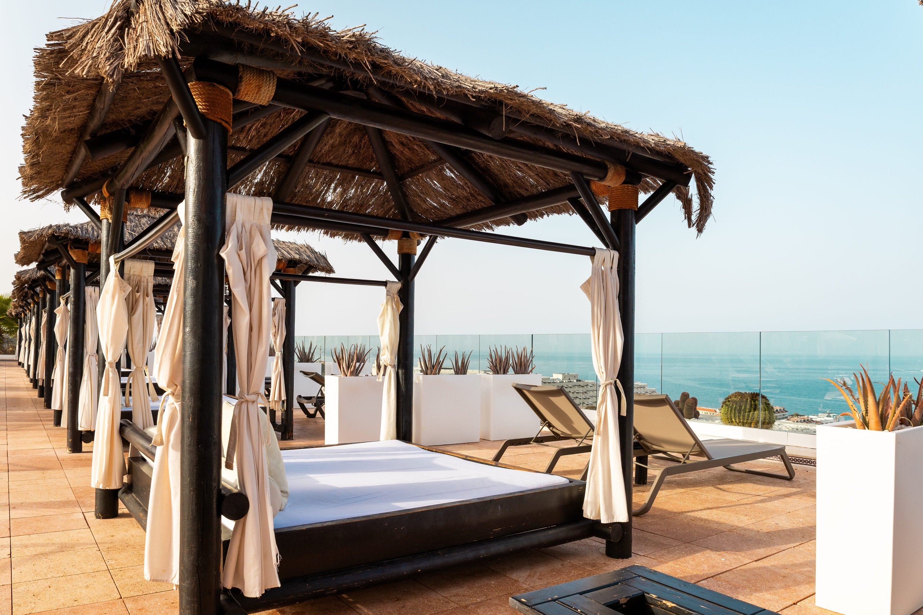 a gazebo with a thatched roof sits on a patio overlooking the ocean