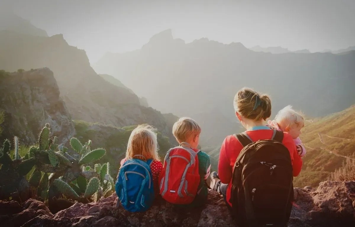 una mujer y dos niños con mochilas miran las montañas