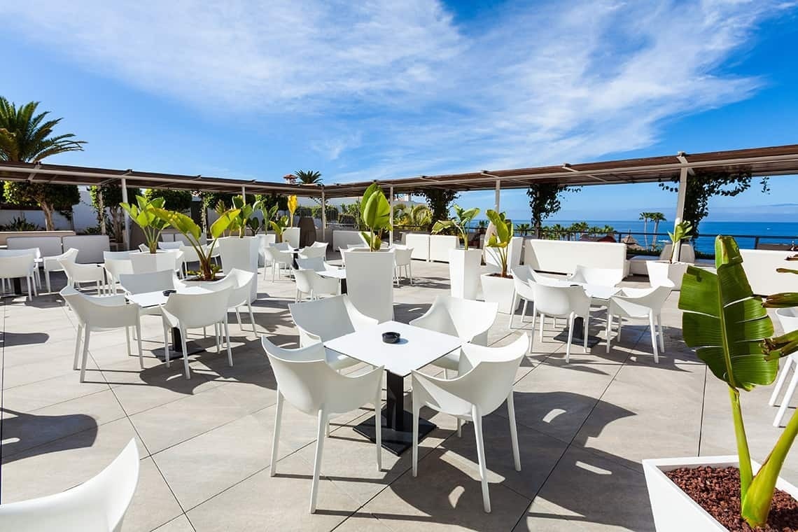 tables and chairs on a patio with a view of the ocean