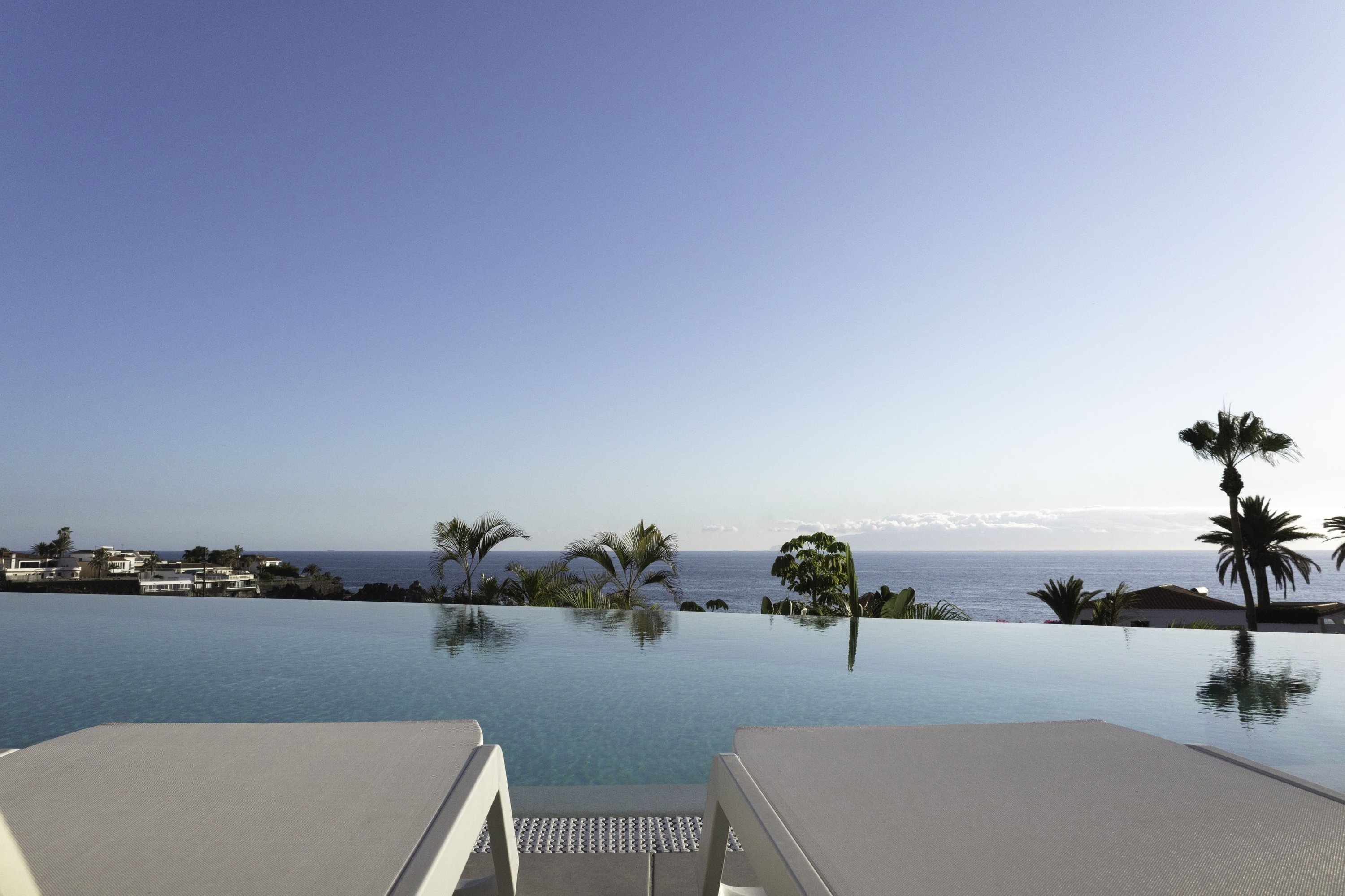 ein Infinity-Pool mit Liegestühlen und Sonnenschirmen umgeben