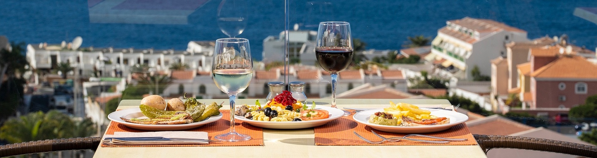 two plates of food and two glasses of wine on a table with a view of the ocean