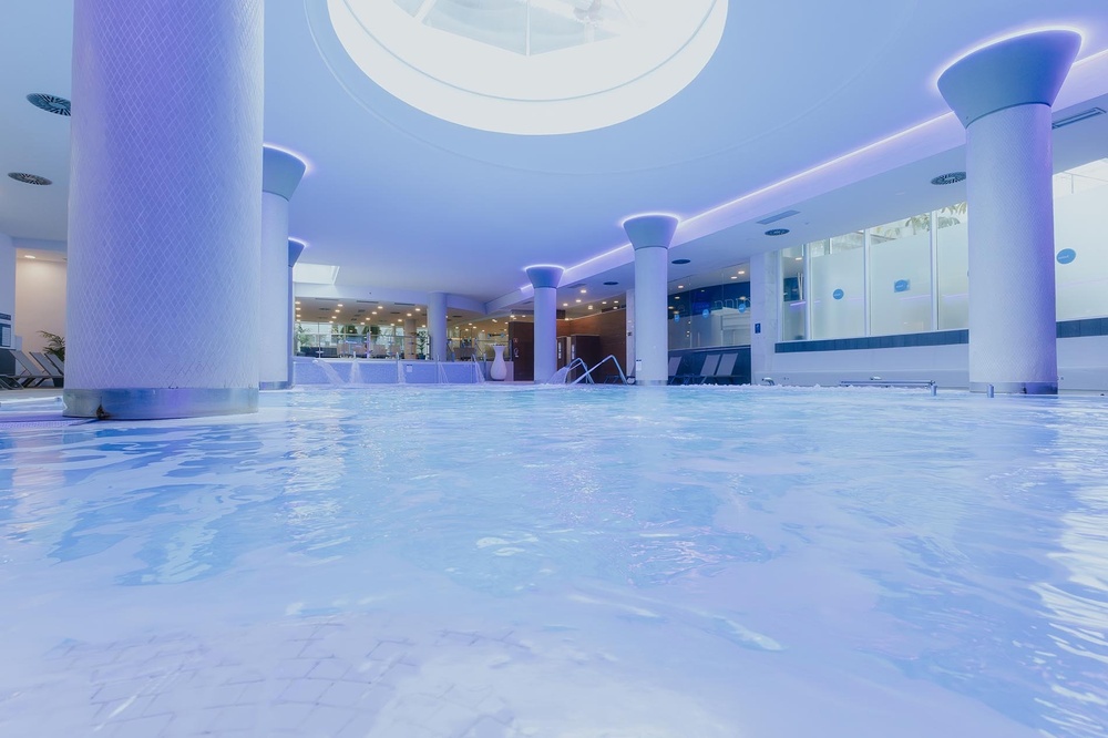 una piscina llena de agua en un spa con columnas blancas y luces moradas