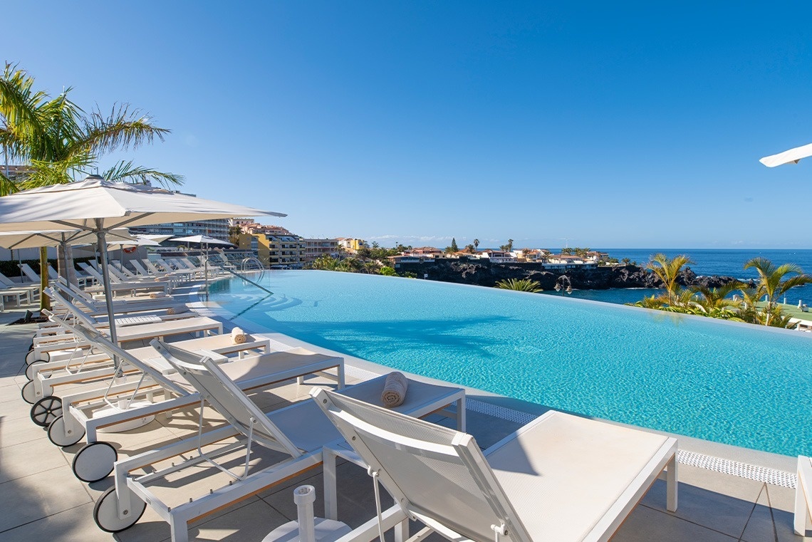 une piscine à débordement est entourée de palmiers et de chaises longues