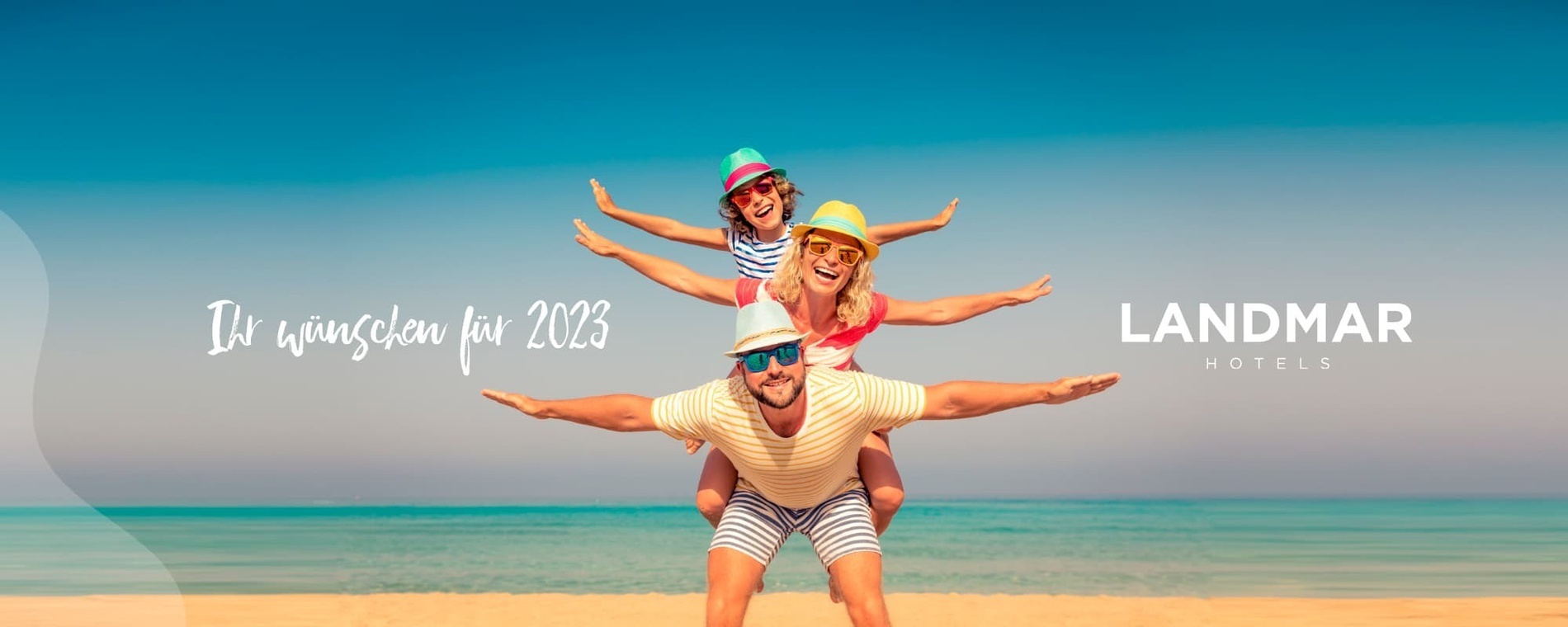 ein Mann trägt eine Frau und ein Kind auf den Schultern am Strand