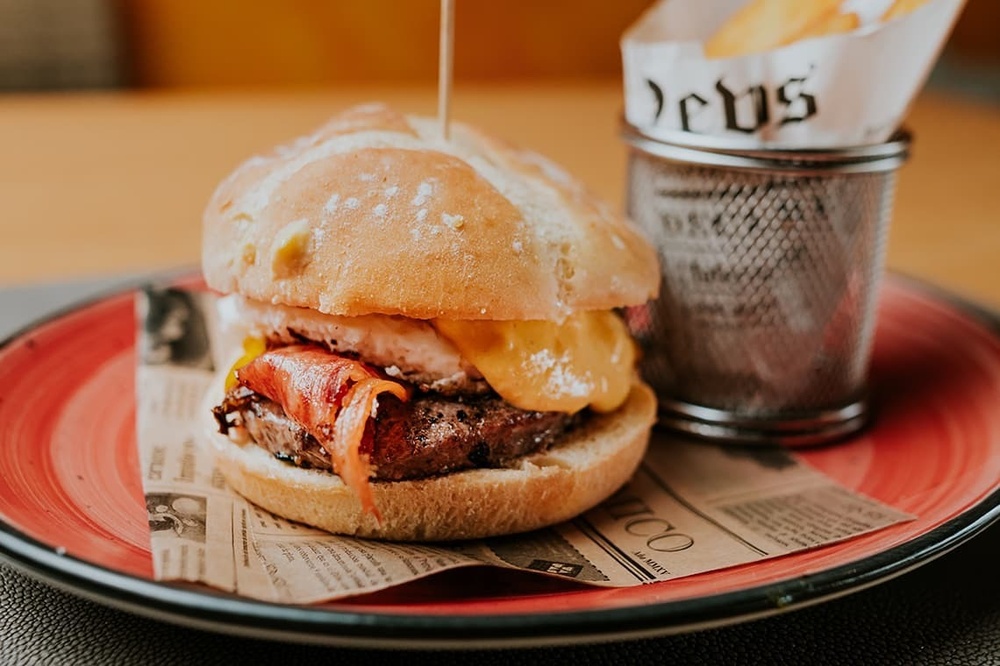 a hamburger on a plate next to a basket that says deus