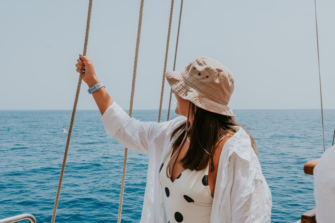 a woman wearing a bucket hat and a white shirt is standing on a boat in the ocean