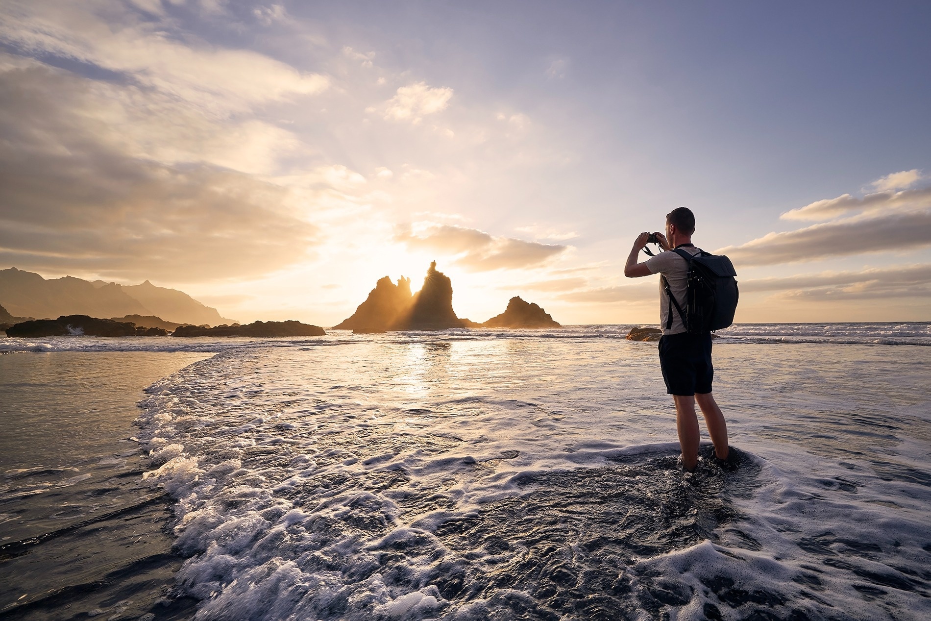 ein Mann steht am Strand und fotografiert den Sonnenuntergang