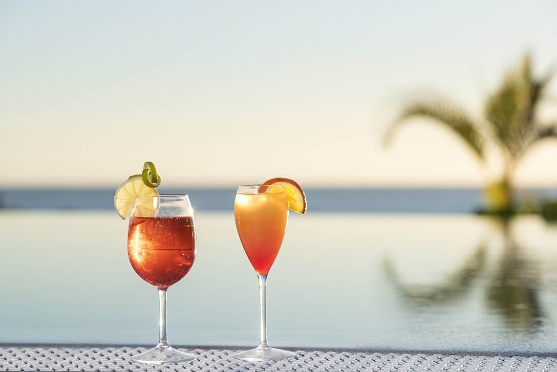 Zwei Gläser mit Cocktails stehen neben einem Pool