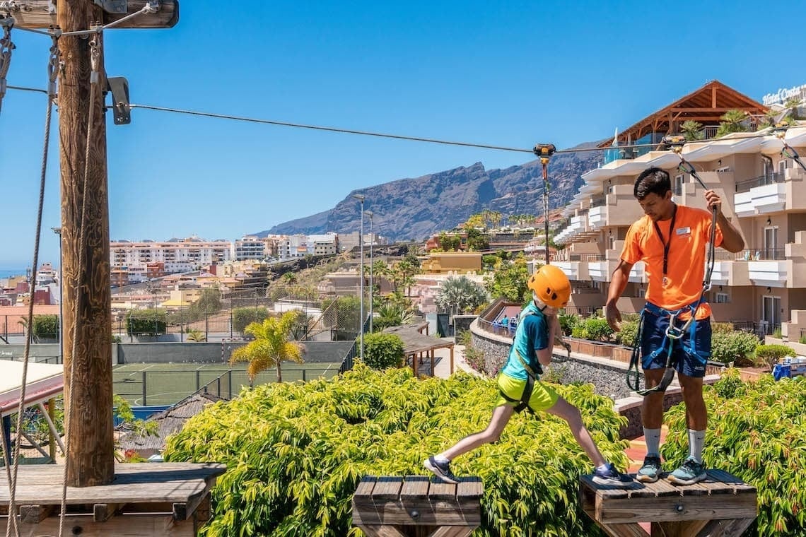 a girl climbs a wooden ropes course with a man watching