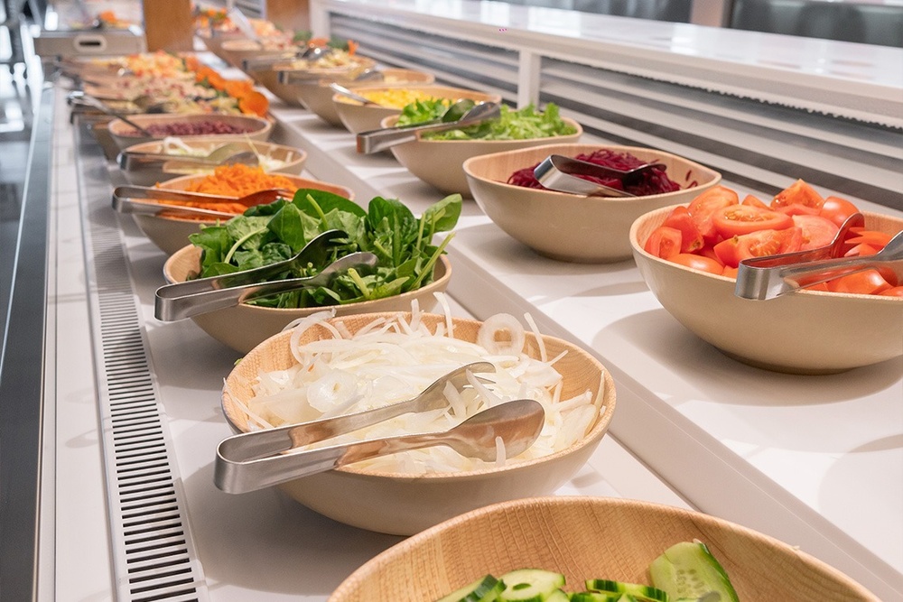a buffet line with bowls of vegetables and tongs