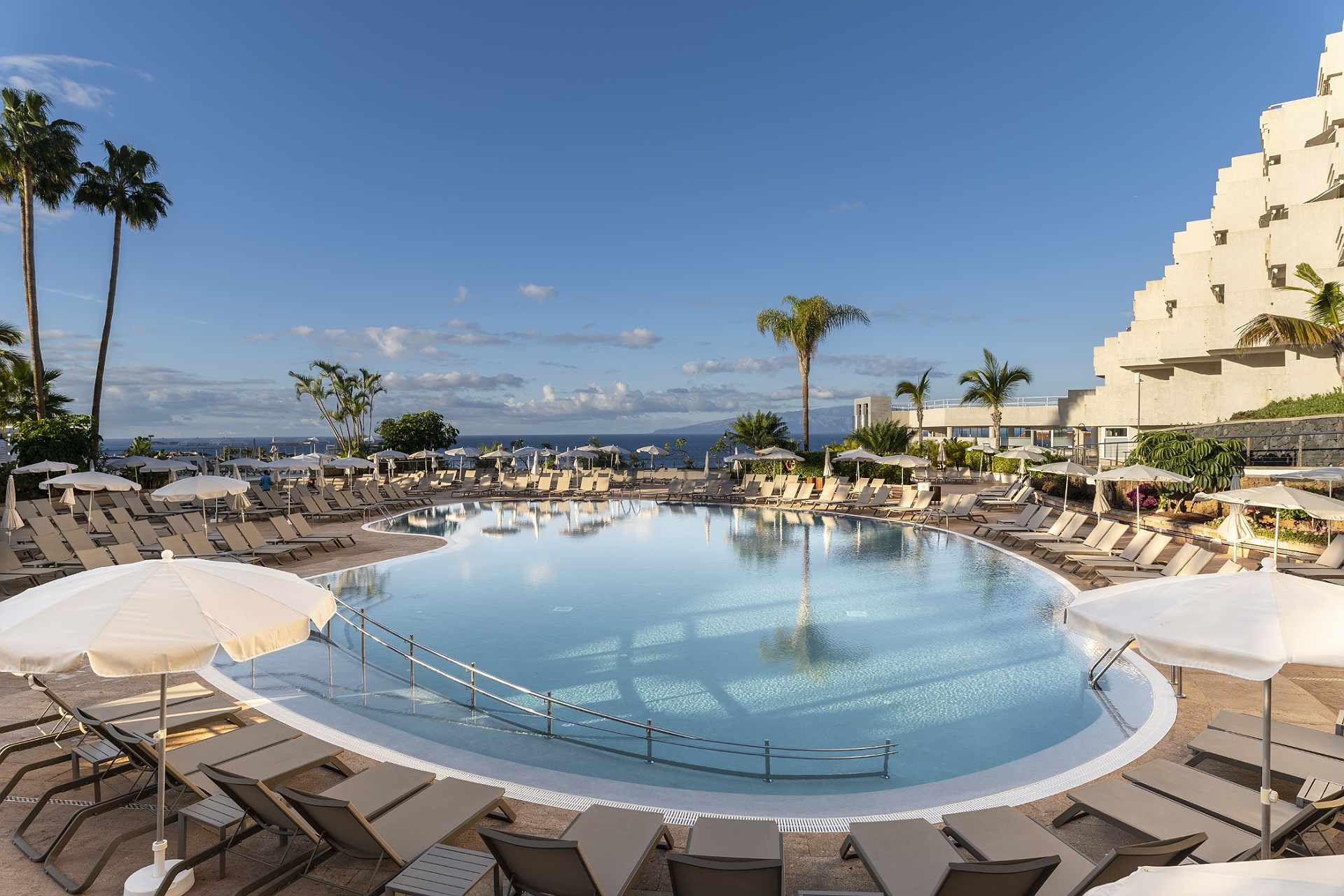 Landmar hotel pool with sun loungers and palm trees, ocean view.