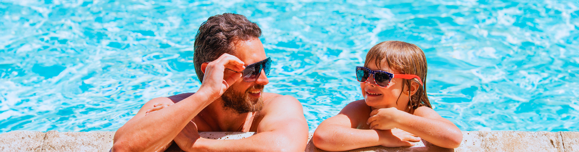 ein Mann und ein kleines Mädchen sitzen an einem Pool und tragen Sonnenbrille