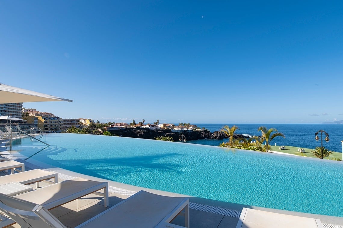 una piscina infinita con vistas al océano está rodeada de sillas y sombrillas