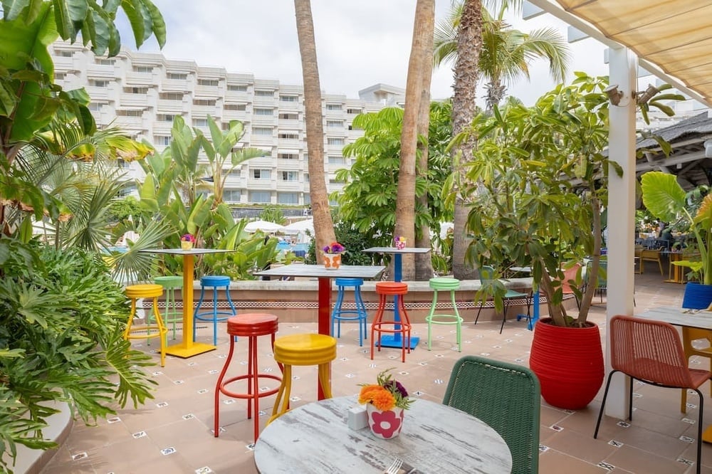 eine Terrasse mit bunten Stühlen und Tischen mit einem Hotel im Hintergrund