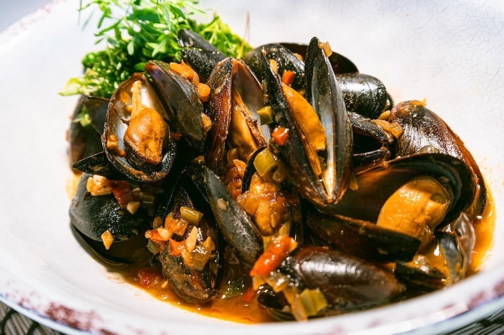 un plato blanco lleno de mejillones y verduras en salsa