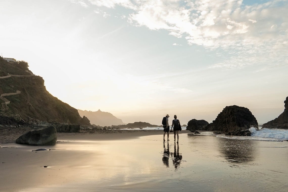 two people standing on a beach looking at the ocean