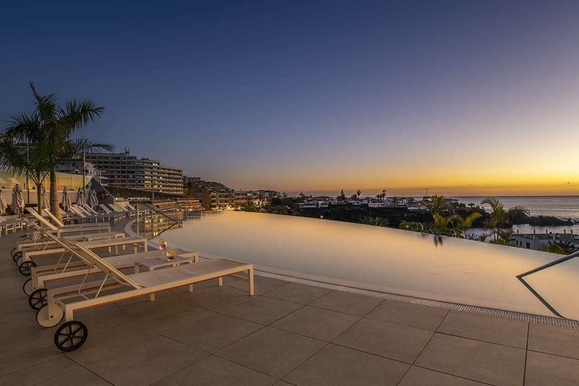 ein Infinity-Pool mit Liegestühlen und Sonnenuntergang im Hintergrund