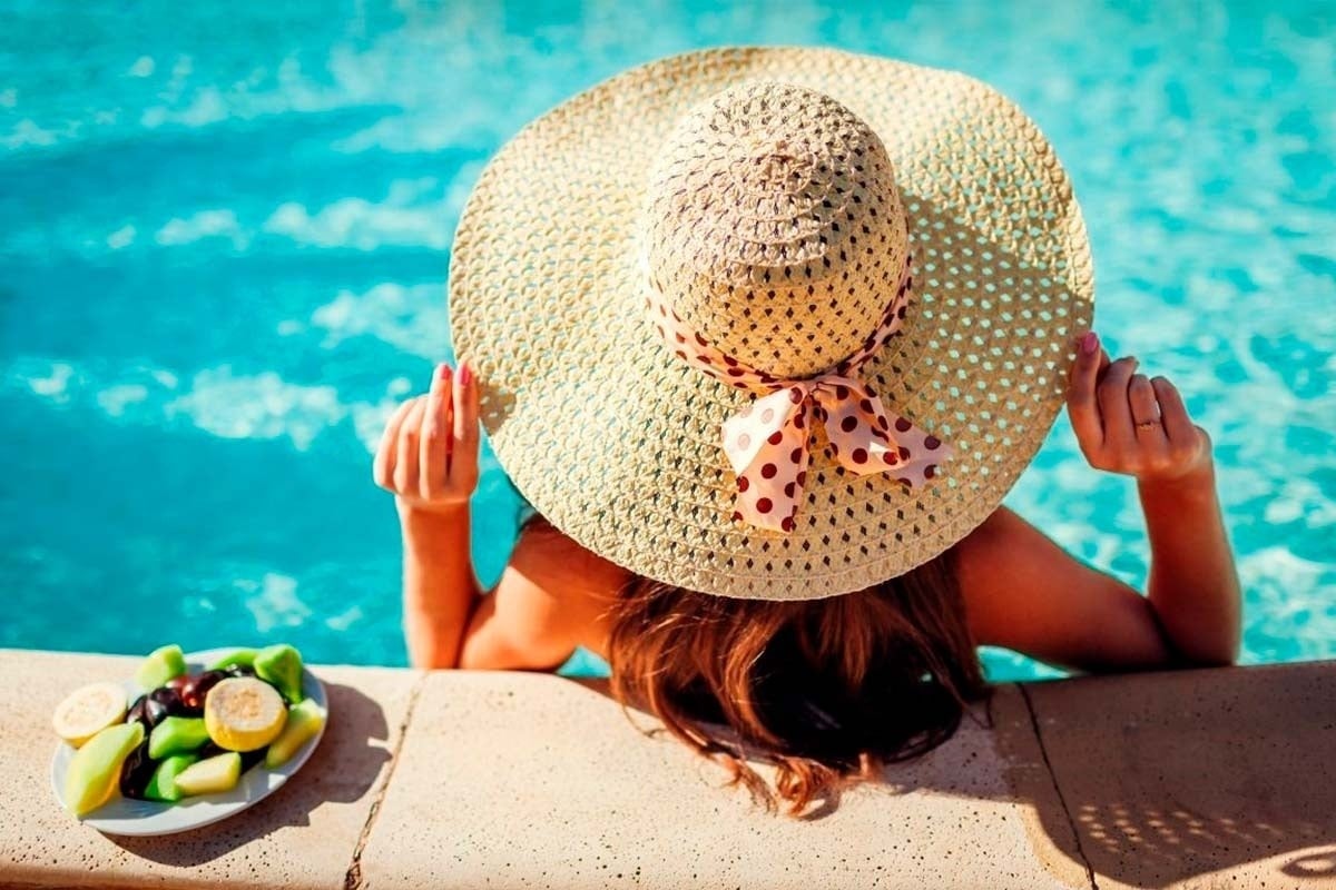 una mujer con un sombrero se sienta junto a una piscina
