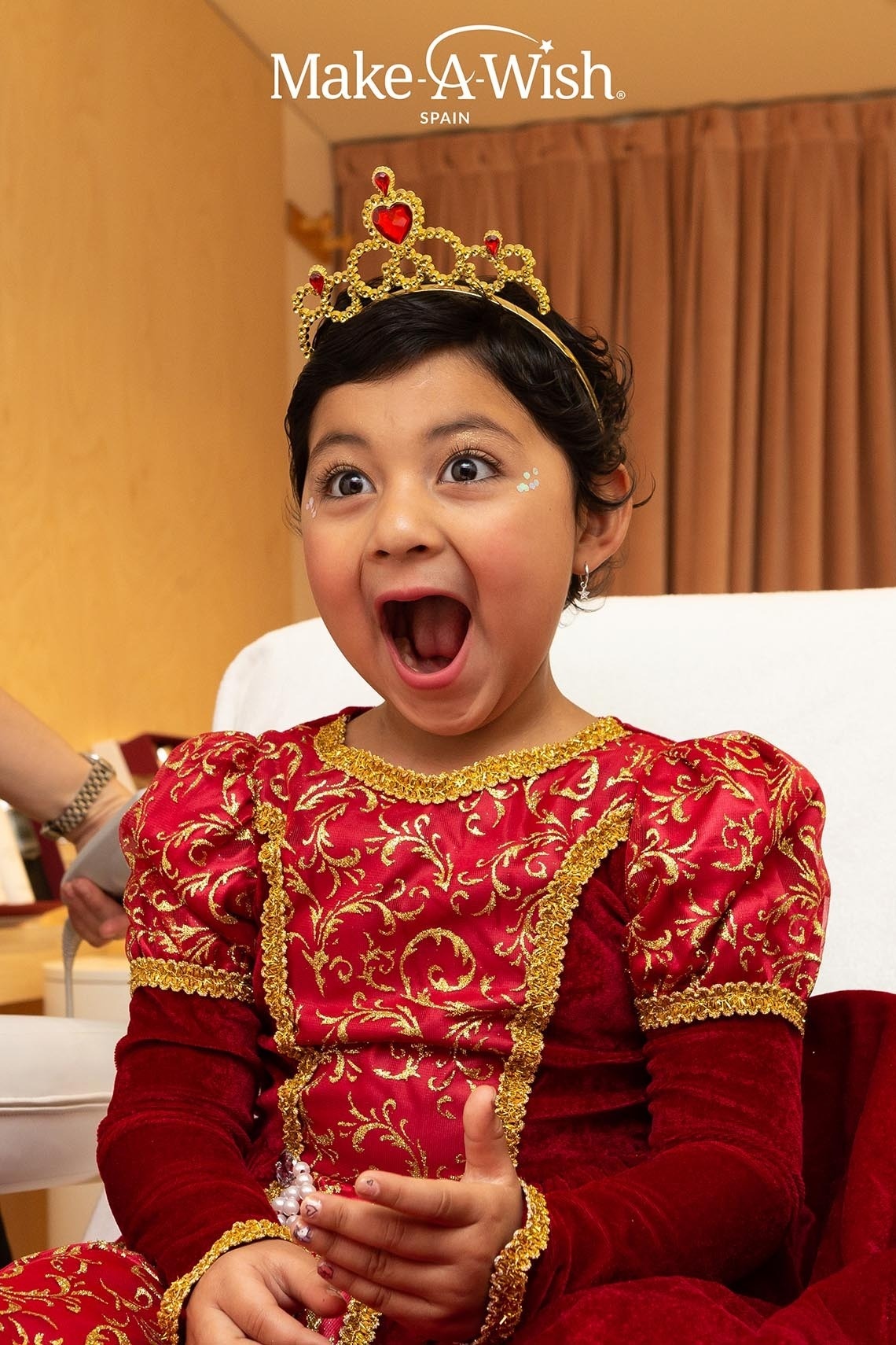 a little girl wearing a red and gold dress and a make a wish advertisement