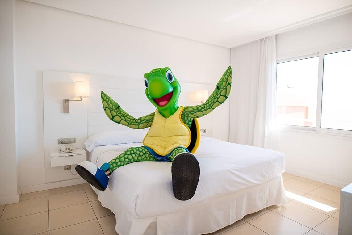 una tortuga de peluche está sentada en una cama blanca