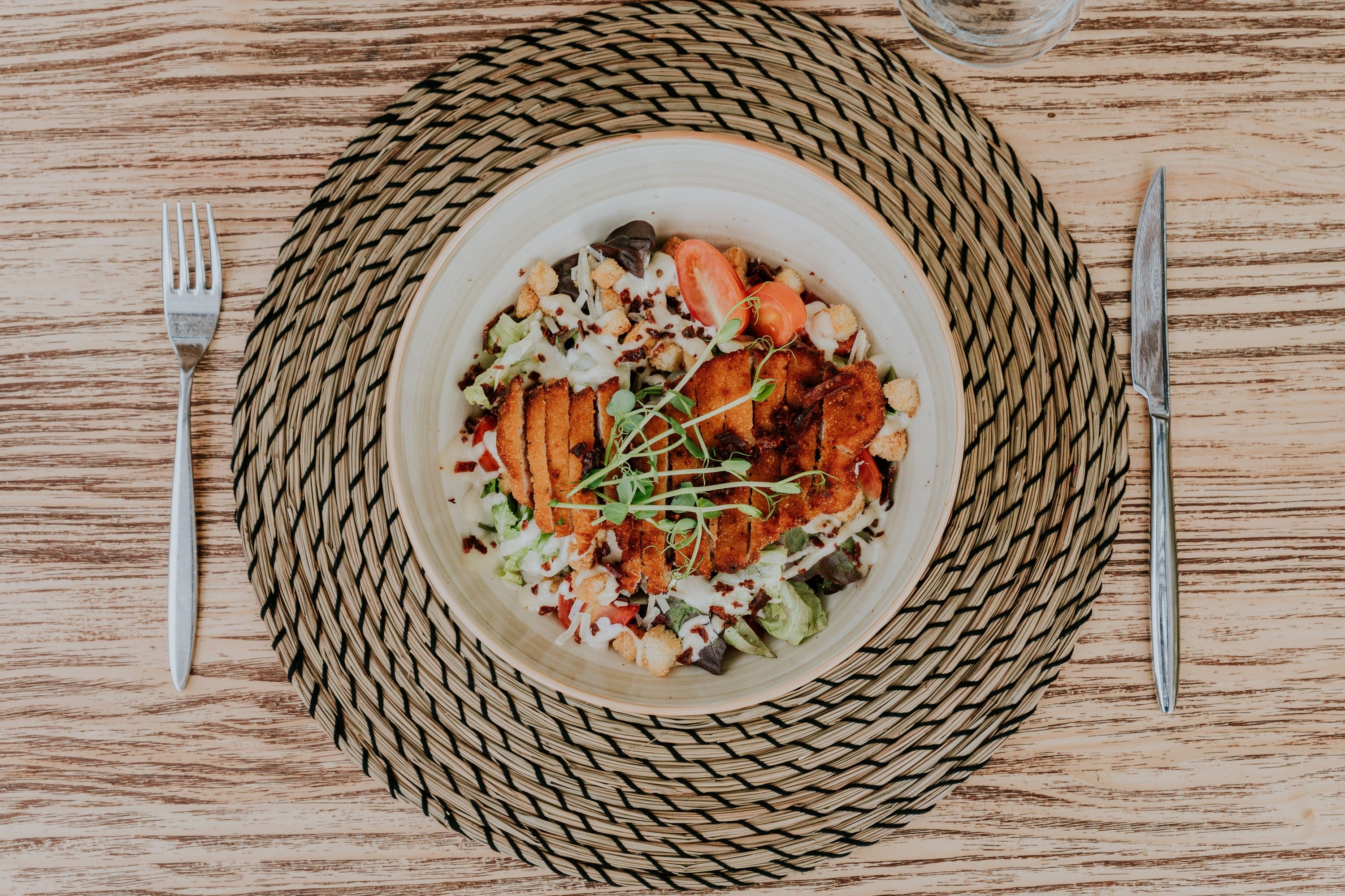 eine Schüssel mit Essen steht auf einem Tisch neben einem Messer und einer Gabel