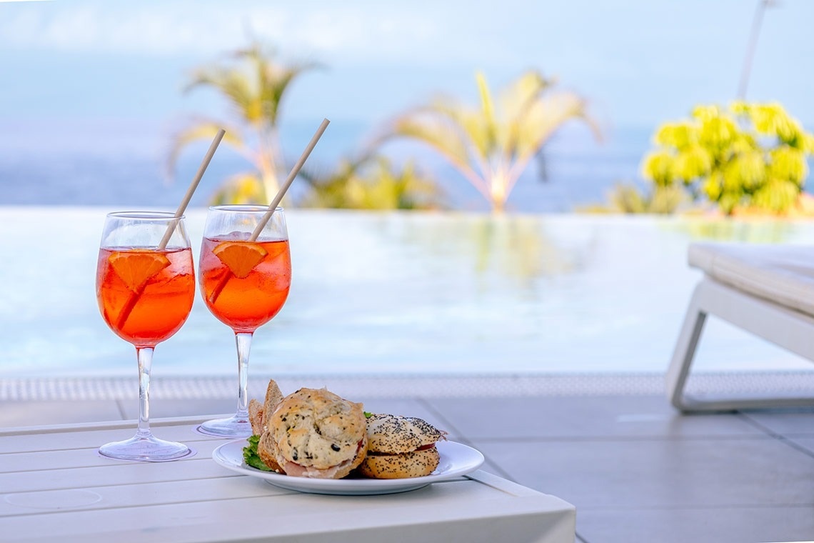 dos copas de vino y un sándwich en una mesa junto a una piscina