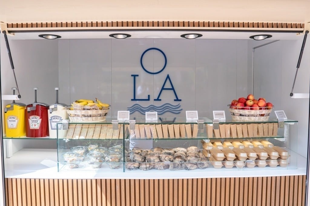 Landmar food counter with sandwiches, fruit, and condiments displayed.