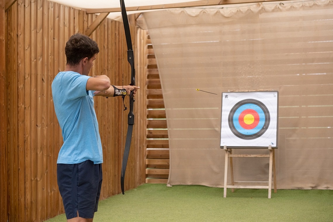 un hombre sostiene un arco y una flecha frente a un objetivo