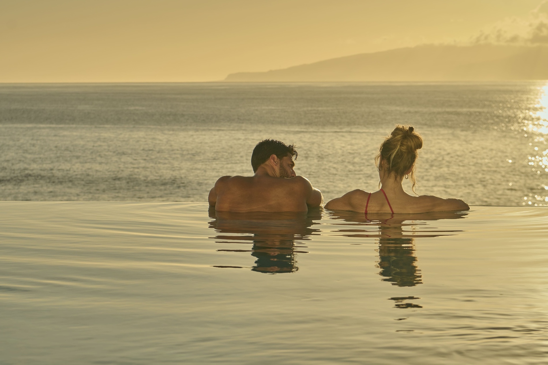 two glasses of champagne sit on a table next to an infinity pool overlooking the ocean