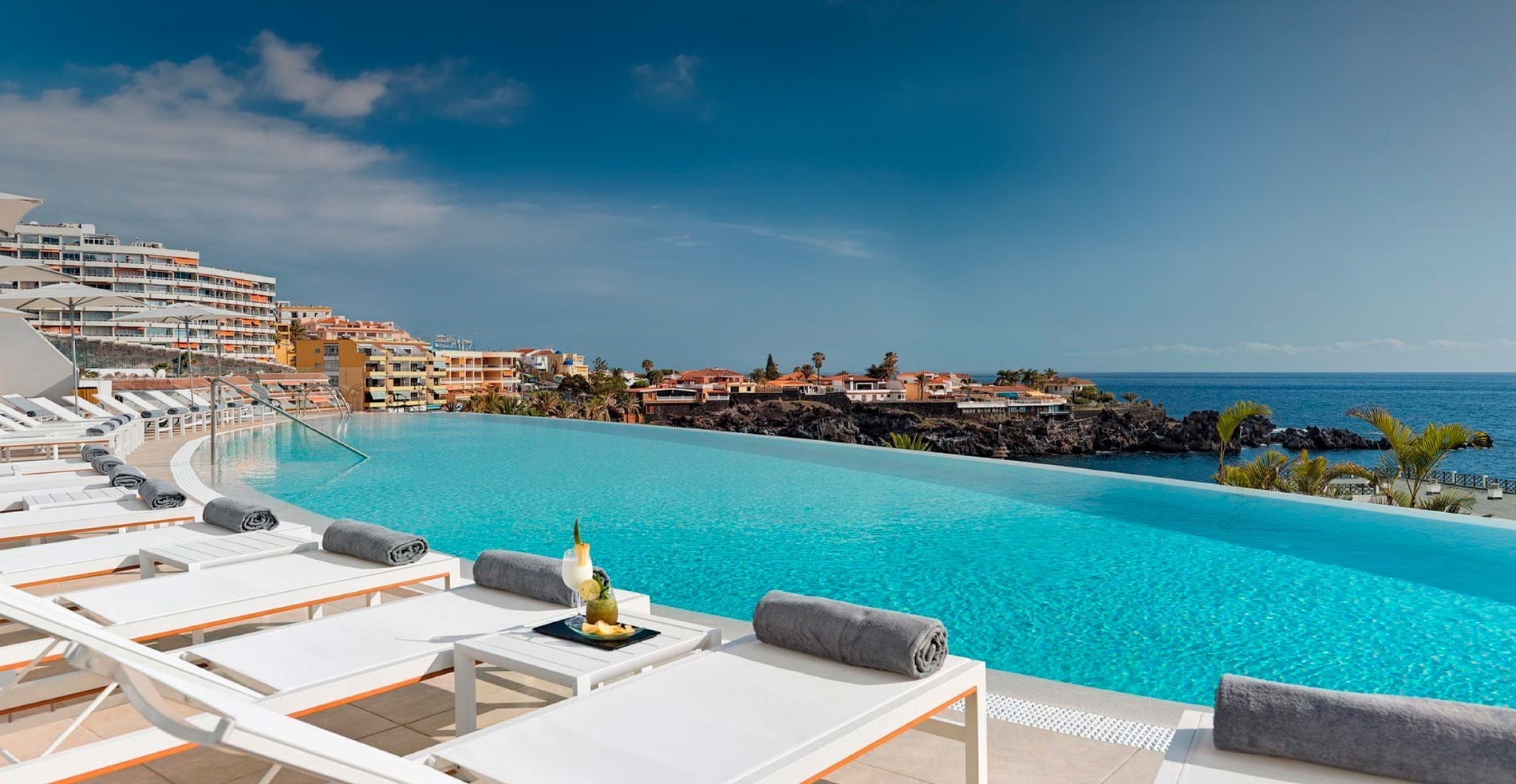 ein Infinity-Pool mit Liegestühlen und Sonnenschirmen umgeben