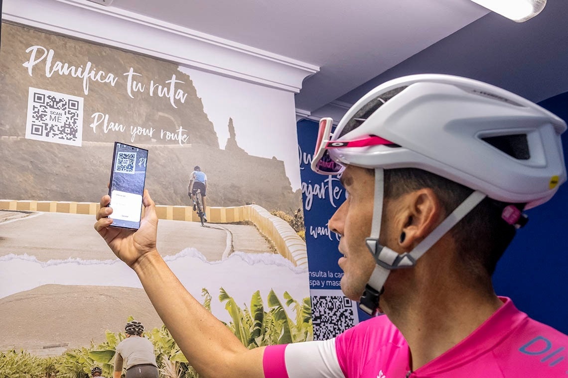un hombre con un casco sostiene un teléfono inteligente frente a un cartel que dice planifica tu ruta