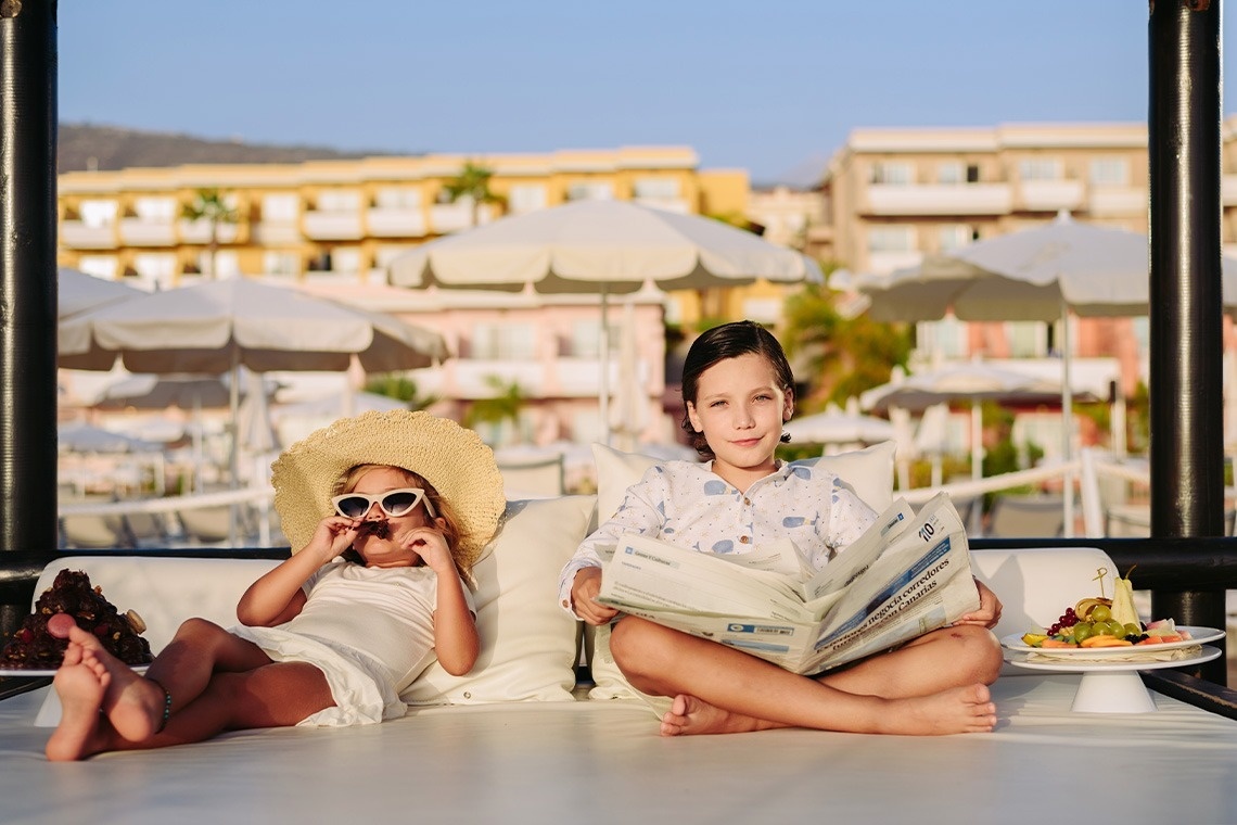 dos niños están sentados en una cama leyendo periódicos