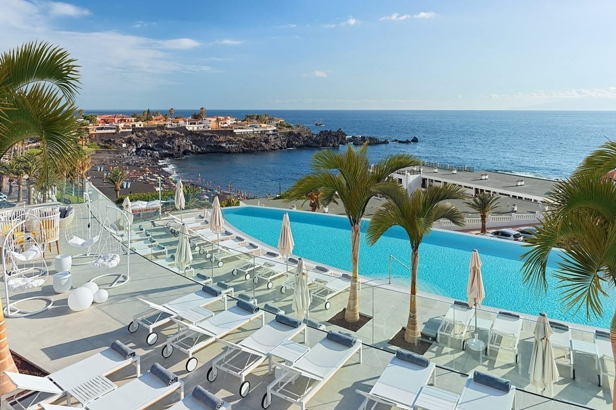 una piscina infinita rodeada de sillas y palmeras con vistas al océano