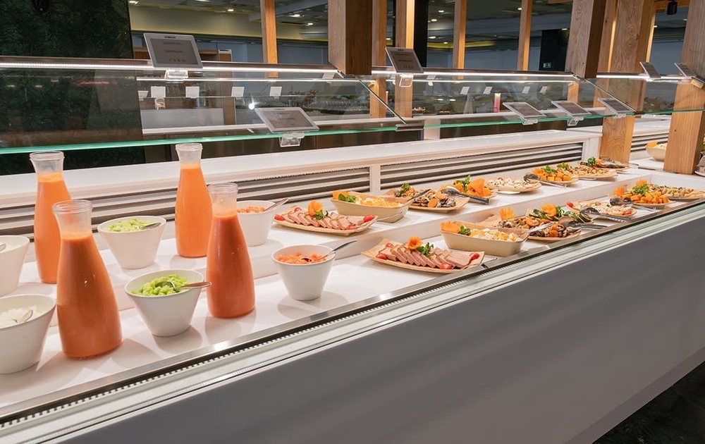 a buffet line with bottles of orange juice and bowls of food