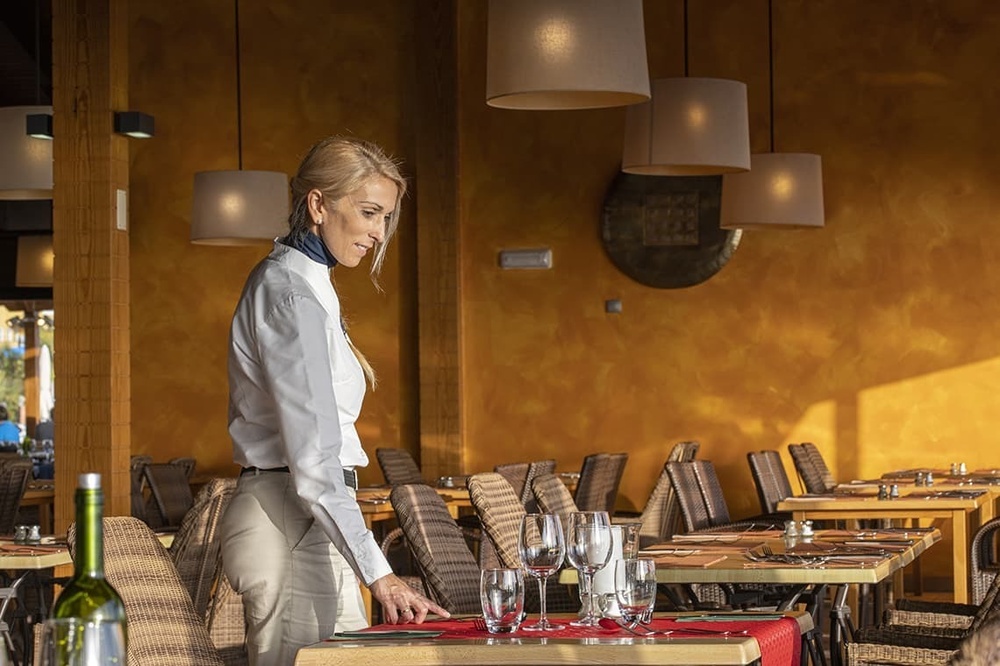 a woman in a white shirt is setting a table in a restaurant