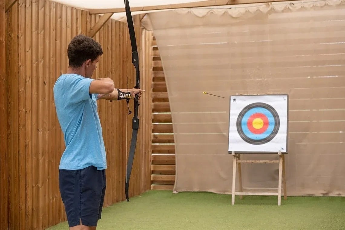 ein Mann hält einen Bogen und einen Pfeil vor einem Ziel