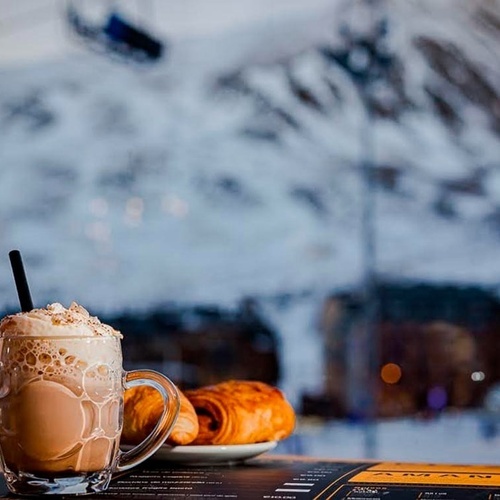 una taza de café y un croissant en una mesa con una montaña en el fondo