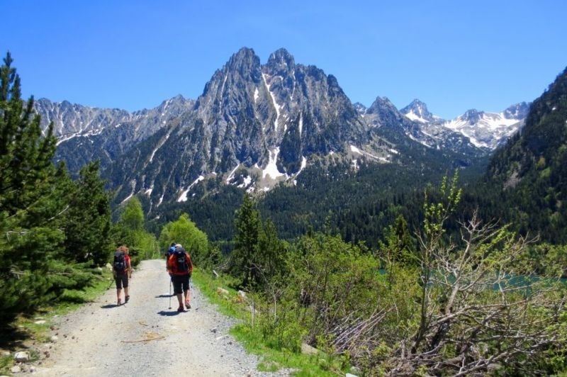 dos personas con mochilas caminan por un camino de tierra con montañas en el fondo
