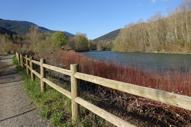 una cerca de madera junto a un río con montañas en el fondo