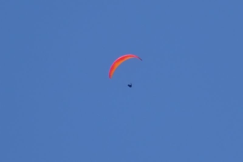 un parapente rojo está volando en un cielo azul claro .