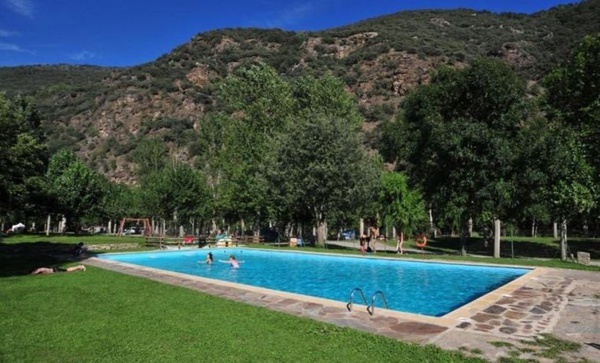 una gran piscina rodeada de hierba y árboles con montañas en el fondo .